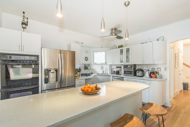 Mid-sized trendy l-shaped porcelain tile and gray floor enclosed kitchen photo in New York with an undermount sink, flat-panel cabinets, white cabinets, quartz countertops, white backsplash, subway tile backsplash, stainless steel appliances, a peninsula and white countertops