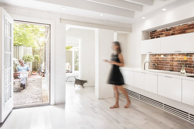 Example of a small minimalist single-wall light wood floor eat-in kitchen design in Boston with an integrated sink, flat-panel cabinets, white cabinets, solid surface countertops, glass sheet backsplash, paneled appliances and no island
