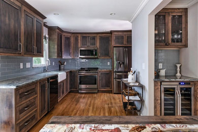 Example of a mid-sized mountain style u-shaped medium tone wood floor and brown floor eat-in kitchen design in Providence with a farmhouse sink, recessed-panel cabinets, dark wood cabinets, granite countertops, blue backsplash, subway tile backsplash, stainless steel appliances, no island and multicolored countertops