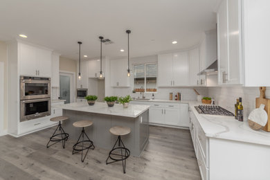 Foto de cocina lineal clásica renovada de tamaño medio abierta con fregadero bajoencimera, armarios estilo shaker, puertas de armario blancas, encimera de cuarcita, salpicadero blanco, salpicadero de azulejos tipo metro, electrodomésticos de acero inoxidable, suelo laminado, una isla, suelo gris y encimeras blancas