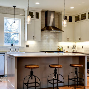 Mid-sized industrial l-shaped eat-in kitchen in Portland with a farmhouse sink, shaker cabinets, white cabinets, quartz benchtops, white splashback, ceramic splashback, stainless steel appliances, medium hardwood floors, with island and brown floor.