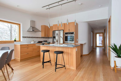 Example of a trendy l-shaped medium tone wood floor and brown floor eat-in kitchen design in Vancouver with an island, shaker cabinets, medium tone wood cabinets, white backsplash, stainless steel appliances and gray countertops
