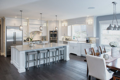 Large transitional l-shaped dark wood floor eat-in kitchen photo in Vancouver with a farmhouse sink, shaker cabinets, white cabinets, quartzite countertops, beige backsplash, stone tile backsplash, stainless steel appliances and an island