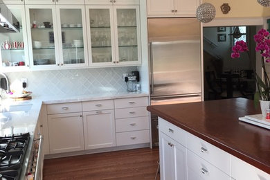 Mid-sized transitional l-shaped medium tone wood floor and brown floor enclosed kitchen photo in San Francisco with shaker cabinets, white cabinets, stainless steel appliances, an island, quartz countertops, white backsplash, glass tile backsplash and white countertops