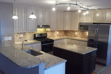 Large trendy l-shaped laminate floor and beige floor enclosed kitchen photo in Chicago with an undermount sink, raised-panel cabinets, white cabinets, granite countertops, beige backsplash, stone tile backsplash, stainless steel appliances and an island