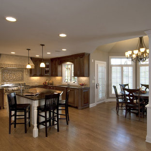 Example of a large classic l-shaped medium tone wood floor open concept kitchen design in Chicago with raised-panel cabinets, dark wood cabinets, beige backsplash, stainless steel appliances and an island