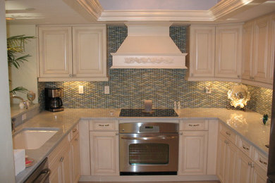 Inspiration for a mid-sized transitional u-shaped ceramic tile enclosed kitchen remodel in Miami with an undermount sink, raised-panel cabinets, white cabinets, granite countertops, multicolored backsplash, mosaic tile backsplash, stainless steel appliances and no island