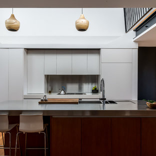 Photo of a contemporary galley kitchen in Other with flat-panel cabinets, white cabinets, stainless steel benchtops, medium hardwood floors, with island, grey floor and grey benchtop.