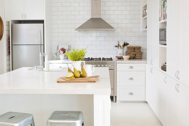 Imagen de cocina de estilo de casa de campo con puertas de armario blancas, salpicadero blanco, salpicadero de azulejos tipo metro, electrodomésticos de acero inoxidable y una isla