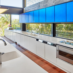 Design ideas for a large contemporary galley open plan kitchen in Sydney with flat-panel cabinets, blue cabinets, solid surface benchtops, panelled appliances, medium hardwood floors, brown floor, an integrated sink, window splashback and with island.