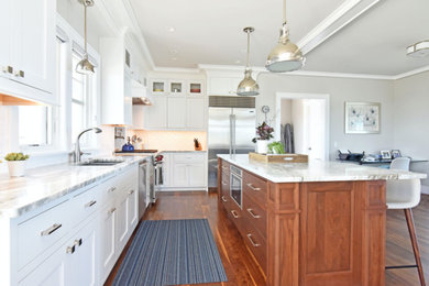 Example of a large transitional l-shaped medium tone wood floor and brown floor open concept kitchen design in Providence with a double-bowl sink, recessed-panel cabinets, white cabinets, marble countertops, white backsplash, subway tile backsplash, stainless steel appliances, an island and white countertops