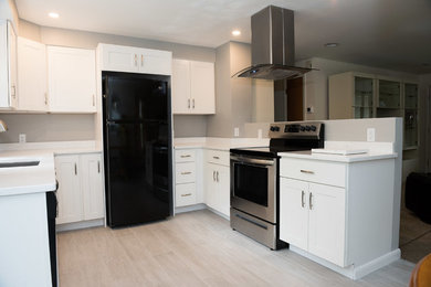 Photo of a medium sized modern u-shaped kitchen/diner in Providence with a submerged sink, shaker cabinets, white cabinets, engineered stone countertops, black appliances, vinyl flooring, a breakfast bar, beige floors and white worktops.