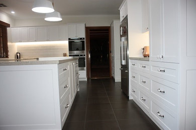 メルボルンにあるモダンスタイルのおしゃれなキッチン (アンダーカウンターシンク、シェーカースタイル扉のキャビネット、白いキャビネット、クオーツストーンカウンター、白いキッチンパネル、サブウェイタイルのキッチンパネル、シルバーの調理設備、黒い床) の写真