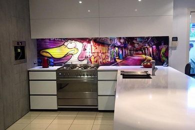 Photo of a large contemporary l-shaped open plan kitchen in Melbourne with an island, a double-bowl sink, flat-panel cabinets, white cabinets, engineered stone countertops, glass sheet splashback, stainless steel appliances, porcelain flooring, beige floors and multi-coloured splashback.