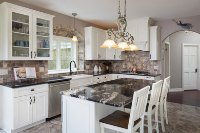 Example of a large classic galley travertine floor and beige floor eat-in kitchen design in Milwaukee with a farmhouse sink, recessed-panel cabinets, white cabinets, marble countertops, beige backsplash, travertine backsplash, stainless steel appliances and an island