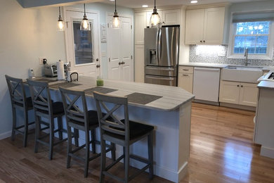 Mid-sized trendy l-shaped light wood floor and beige floor eat-in kitchen photo in Boston with a farmhouse sink, white cabinets, quartzite countertops, multicolored backsplash, mosaic tile backsplash, white appliances, a peninsula and gray countertops