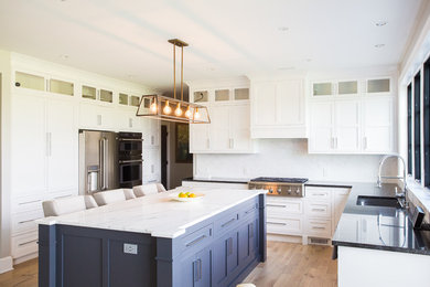 Mid-sized transitional u-shaped medium tone wood floor and brown floor eat-in kitchen photo in Baltimore with an undermount sink, shaker cabinets, white cabinets, marble countertops, white backsplash, marble backsplash, stainless steel appliances, an island and white countertops