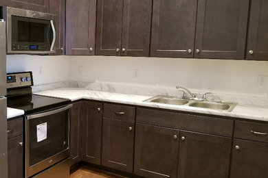 Example of a small transitional l-shaped dark wood floor and brown floor kitchen design in Other with a double-bowl sink, recessed-panel cabinets, dark wood cabinets, laminate countertops, white backsplash, stainless steel appliances and white countertops