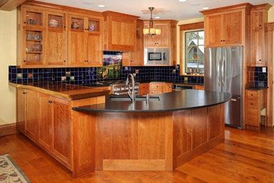 デンバーにあるトラディショナルスタイルのおしゃれなキッチン (中間色木目調キャビネット、シルバーの調理設備、ドロップインシンク、フラットパネル扉のキャビネット、ライムストーンカウンター、黒いキッチンパネル、ガラスタイルのキッチンパネル、無垢フローリング) の写真