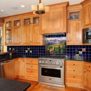 This is an example of an arts and crafts u-shaped eat-in kitchen in Denver with a drop-in sink, flat-panel cabinets, medium wood cabinets, limestone benchtops, black splashback, glass tile splashback, stainless steel appliances, medium hardwood floors and with island.