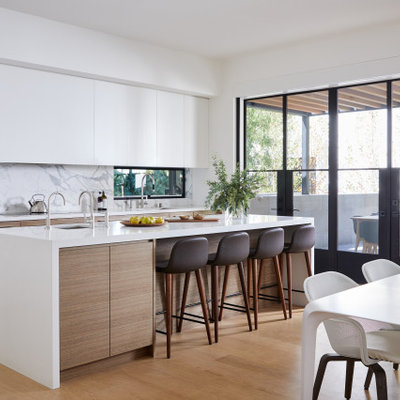 Inspiration for a modern galley medium tone wood floor and brown floor kitchen remodel in San Francisco with flat-panel cabinets, white cabinets, white backsplash, paneled appliances, an island and white countertops