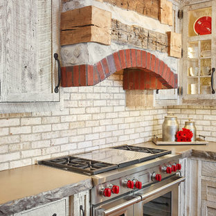 Mid-sized rustic eat-in kitchen designs - Example of a mid-sized mountain style medium tone wood floor and brown floor eat-in kitchen design in Grand Rapids with a farmhouse sink, glass-front cabinets, distressed cabinets, concrete countertops, beige backsplash, brick backsplash, stainless steel appliances and an island