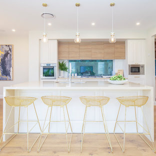 Contemporary eat-in kitchen in Sydney with an undermount sink, raised-panel cabinets, white cabinets, window splashback, stainless steel appliances, light hardwood floors, with island, beige floor and white benchtop.