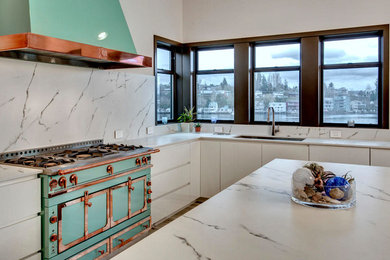 Trendy l-shaped porcelain tile open concept kitchen photo in Seattle with a single-bowl sink, flat-panel cabinets, white cabinets, solid surface countertops, yellow backsplash, limestone backsplash, paneled appliances, an island and white countertops