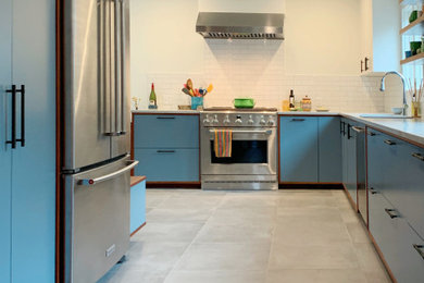 Mid-sized trendy l-shaped ceramic tile and gray floor kitchen photo in Portland with an undermount sink, flat-panel cabinets, blue cabinets, solid surface countertops, white backsplash, ceramic backsplash, stainless steel appliances, no island and gray countertops