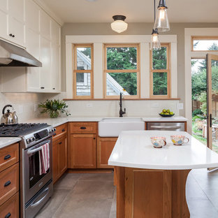 Photo of a mid-sized arts and crafts l-shaped separate kitchen in Portland with a farmhouse sink, medium wood cabinets, quartz benchtops, white splashback, ceramic splashback, stainless steel appliances, ceramic floors, with island, recessed-panel cabinets and grey floor.