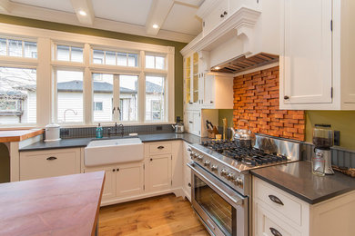 Klassische Küche in L-Form mit Landhausspüle, weißen Schränken, Quarzit-Arbeitsplatte, Küchenrückwand in Grau, hellem Holzboden und Kücheninsel in Portland