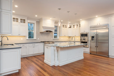 Inspiration for a large timeless l-shaped medium tone wood floor and brown floor kitchen remodel in Boston with an undermount sink, beaded inset cabinets, white cabinets, soapstone countertops, gray backsplash, ceramic backsplash, stainless steel appliances, an island and gray countertops
