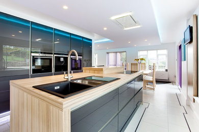 This is an example of a large modern u-shaped open plan kitchen in Other with a double-bowl sink, flat-panel cabinets, grey cabinets, wood worktops, black appliances, ceramic flooring and an island.