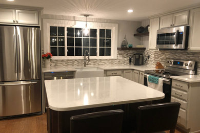 Example of a mid-sized transitional l-shaped medium tone wood floor and brown floor eat-in kitchen design in Boston with a farmhouse sink, recessed-panel cabinets, white cabinets, quartz countertops, multicolored backsplash, mosaic tile backsplash, stainless steel appliances, an island and white countertops