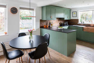 Design ideas for a medium sized traditional u-shaped kitchen/diner in Kent with a belfast sink, shaker cabinets, green cabinets, engineered stone countertops, metal splashback, lino flooring, a breakfast bar and green floors.