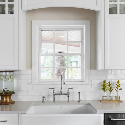 Eat-in kitchen - mid-sized transitional l-shaped medium tone wood floor eat-in kitchen idea in Minneapolis with a farmhouse sink, white cabinets, white backsplash, subway tile backsplash, stainless steel appliances, an island, shaker cabinets and quartzite countertops