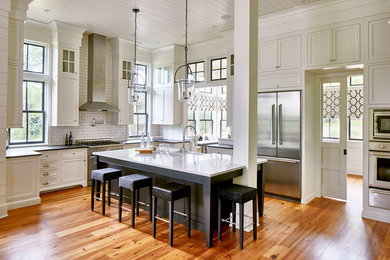 Large farmhouse l-shaped medium tone wood floor and brown floor kitchen photo in Atlanta with a farmhouse sink, shaker cabinets, white cabinets, white backsplash, subway tile backsplash, stainless steel appliances, an island, black countertops and solid surface countertops