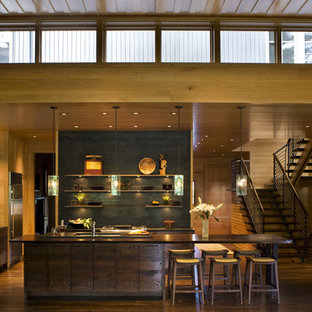 Inspiration for a transitional galley open plan kitchen in Charlotte with flat-panel cabinets, dark wood cabinets, black splashback, with island, a drop-in sink, metal splashback, stainless steel appliances, dark hardwood floors and brown floor.