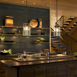 Modelo de cocina comedor actual, de tamaño medio, con una isla, armarios con paneles lisos, puertas de armario de madera en tonos medios, encimera de madera, salpicadero negro, salpicadero de metal, suelo de madera oscura, fregadero encastrado, electrodomésticos de acero inoxidable y suelo marrón