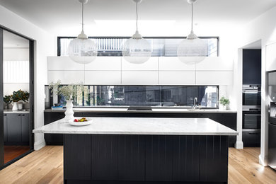 Bild på ett stort funkis grå grått l-kök, med en undermonterad diskho, marmorbänkskiva, fönster som stänkskydd, ljust trägolv, en köksö, släta luckor, svarta skåp, rostfria vitvaror och beiget golv