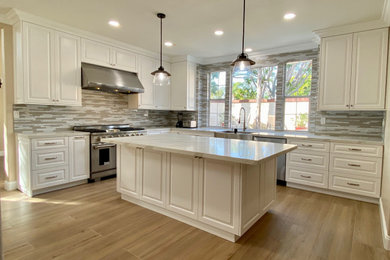 Kitchen - traditional l-shaped vinyl floor kitchen idea in Orange County with raised-panel cabinets, white cabinets, quartz countertops, mosaic tile backsplash, stainless steel appliances and an island