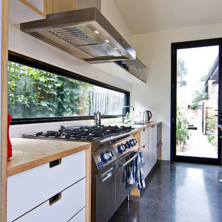 Inspiration for a large industrial galley eat-in kitchen in Melbourne with a double-bowl sink, flat-panel cabinets, white cabinets, wood benchtops, white splashback, glass sheet splashback, stainless steel appliances, concrete floors and with island.