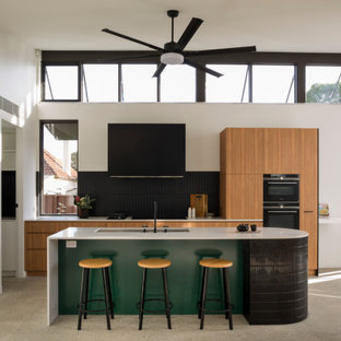 Inspiration for a mid-sized contemporary galley open plan kitchen in Sydney with an undermount sink, medium wood cabinets, black splashback, ceramic splashback, black appliances, concrete floors, with island, grey floor and white benchtop.