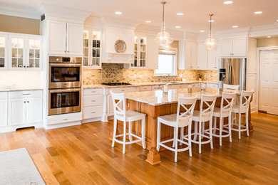 Example of a mid-sized transitional l-shaped medium tone wood floor and brown floor open concept kitchen design in Chicago with an undermount sink, raised-panel cabinets, white cabinets, granite countertops, stainless steel appliances, an island, beige backsplash and travertine backsplash