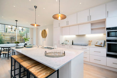 Medium sized contemporary l-shaped open plan kitchen in London with flat-panel cabinets, white cabinets and an island.