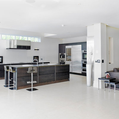 Example of a huge minimalist l-shaped gray floor open concept kitchen design with an undermount sink, flat-panel cabinets, dark wood cabinets, stainless steel appliances, an island and gray countertops
