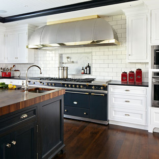 Foto de cocina clásica renovada con armarios estilo shaker, puertas de armario blancas, salpicadero blanco, salpicadero de azulejos tipo metro, suelo de madera oscura y electrodomésticos negros