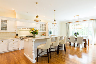 Example of a mid-sized transitional u-shaped medium tone wood floor and brown floor eat-in kitchen design in New Orleans with a drop-in sink, raised-panel cabinets, white cabinets, quartzite countertops, beige backsplash, ceramic backsplash, stainless steel appliances and an island
