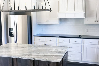 Example of a mid-sized transitional l-shaped porcelain tile and brown floor open concept kitchen design in Austin with a double-bowl sink, shaker cabinets, white cabinets, solid surface countertops, white backsplash, subway tile backsplash, stainless steel appliances, an island and black countertops
