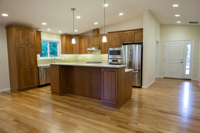 Mid-sized elegant l-shaped medium tone wood floor and brown floor open concept kitchen photo in Seattle with an undermount sink, stainless steel appliances, an island, raised-panel cabinets, dark wood cabinets, quartz countertops, beige backsplash, white countertops and glass tile backsplash
